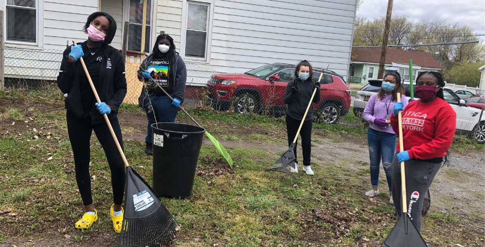 Utica Academy of Science high school students volunteer their time to assist an elderly community member with light yard work as part of their Community Organization initiative.
